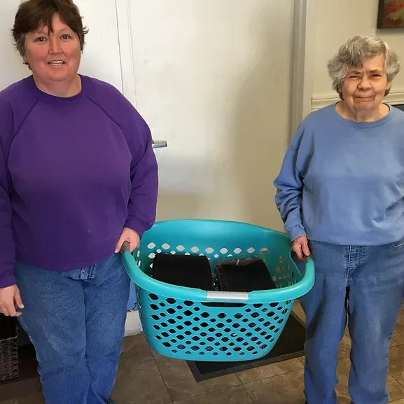 two doco workers carrying a laundry basket between them